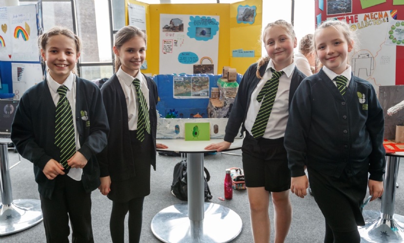 A group of young students in school uniform stand smiling in front of a handmade model of the coast.