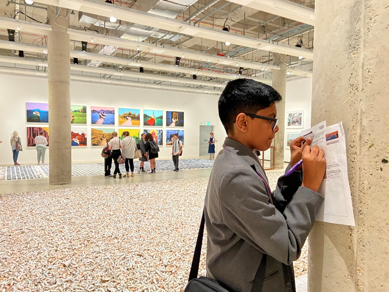 A student writes on a piece of paper against a wall.