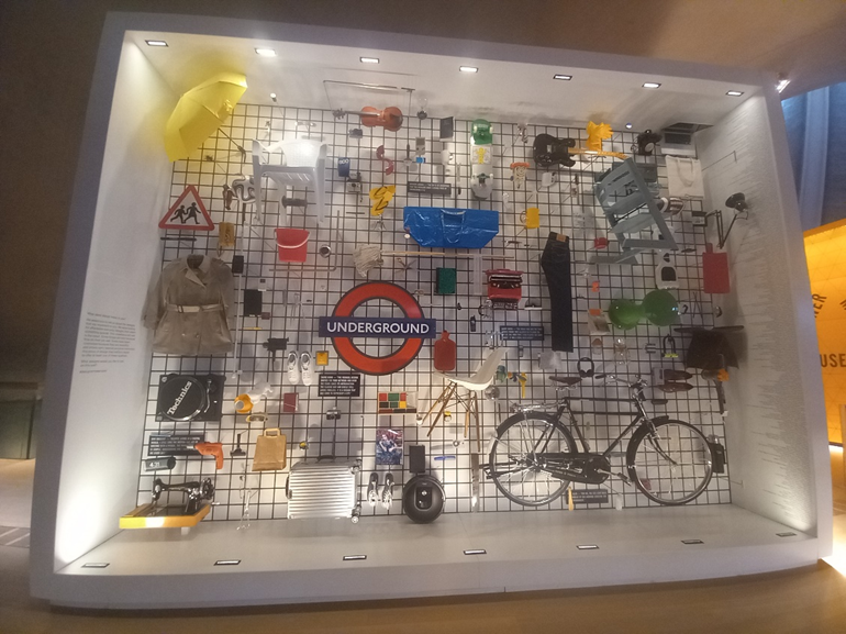 A wall display of objects including a bicycle, a London underground sign, an IKEA bag, and a guitar.