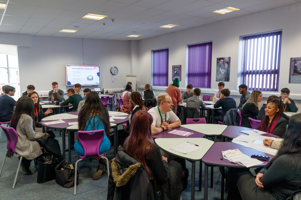 Groups of students sit around tables working together