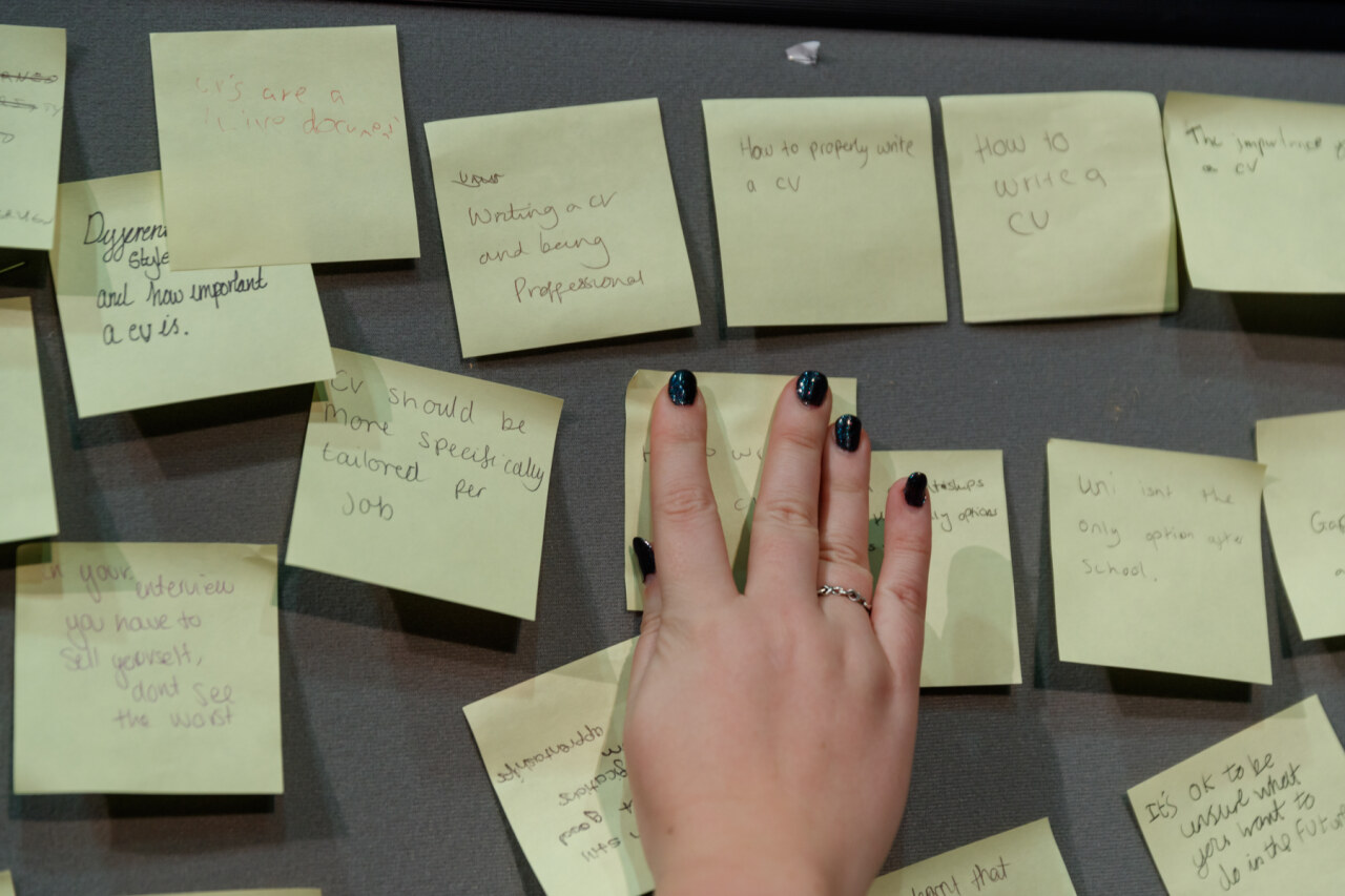 Yellow post it notes being placed on a board by a hand with painted nails