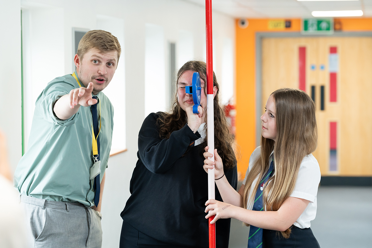 Photo of Maths teacher teaching a practical surveying task to two students