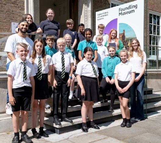 A group of young students in school uniform, and three adults, stand on the steps of a house identified as The Foundling Museum