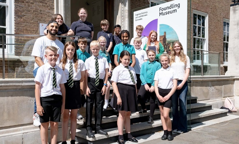 A group of young students in school uniform, and three adults, stand on the steps of a house identified as The Foundling Museum