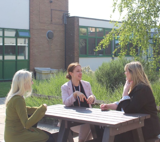 Photo of three members of staff sitting around a picnic table, coaching each other