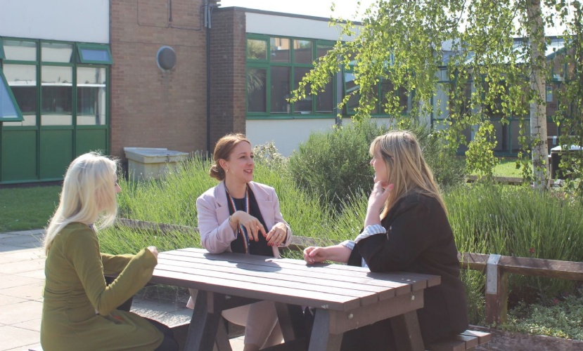 Photo of three members of staff sitting around a picnic table, coaching each other